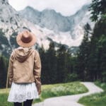 Beautiful young woman stands on road and looking at mountains. Hiker girl enjoys view on Alps and beauty of wild nature outdoors. Adventure travel in Slovenia, Europe. Freedom Natural Lifestyle